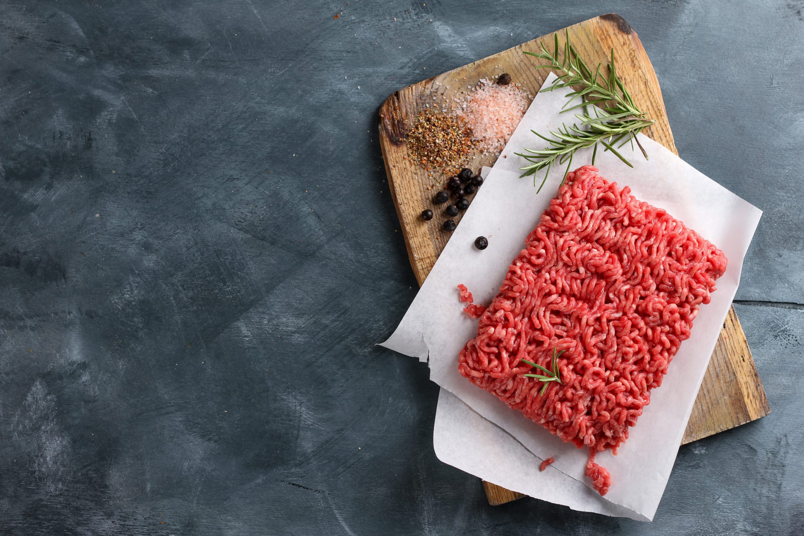 Minced meat on butcher paper with spices and rosemary, selective focus